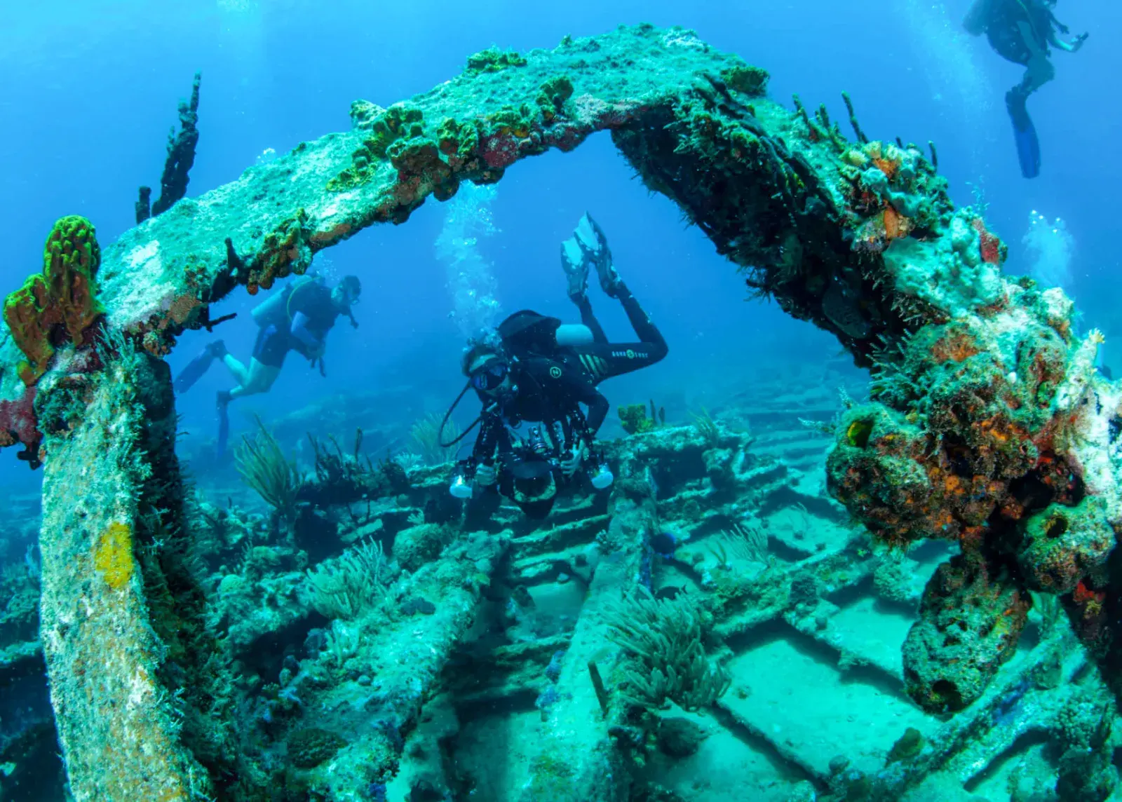 Scuba divers exploring a coral-encrusted shipwreck arch in clear blue water off St. John, US Virgin Islands