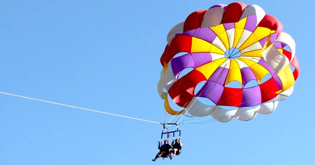 Two people parasailing with a colorful red yellow and purple parachute against a clear blue sky