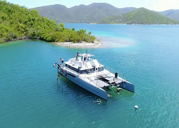 Catamaran anchored in crystal-clear waters off St. John USVI with guests swimming and snorkeling
