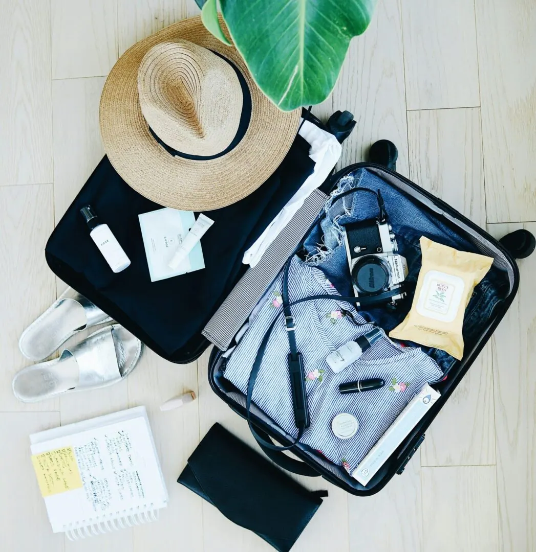 Flat lay of open suitcase packed for vacation with straw hat, camera, sandals, and travel essentials