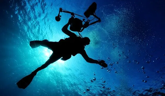 Silhouette of a scuba diver with underwater camera equipment against deep blue ocean water with sunlight and bubbles