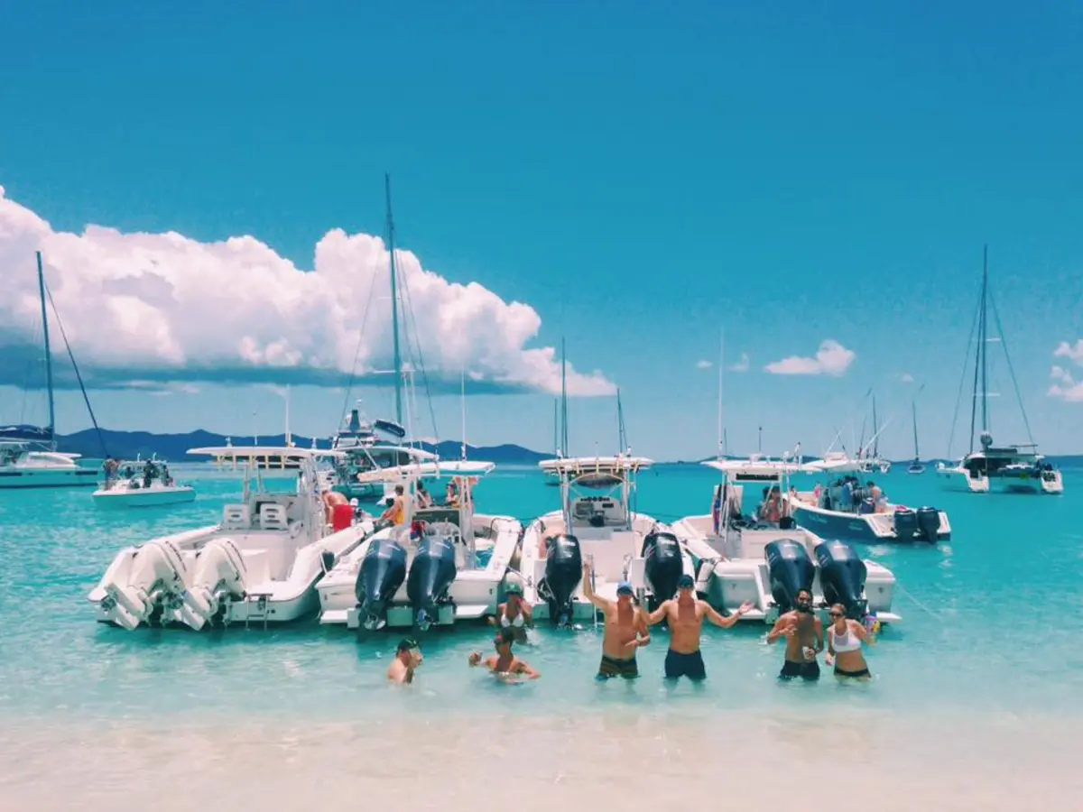 Group of friends standing in turquoise water with powerboats anchored at a sandy beach in St. Thomas, USVI